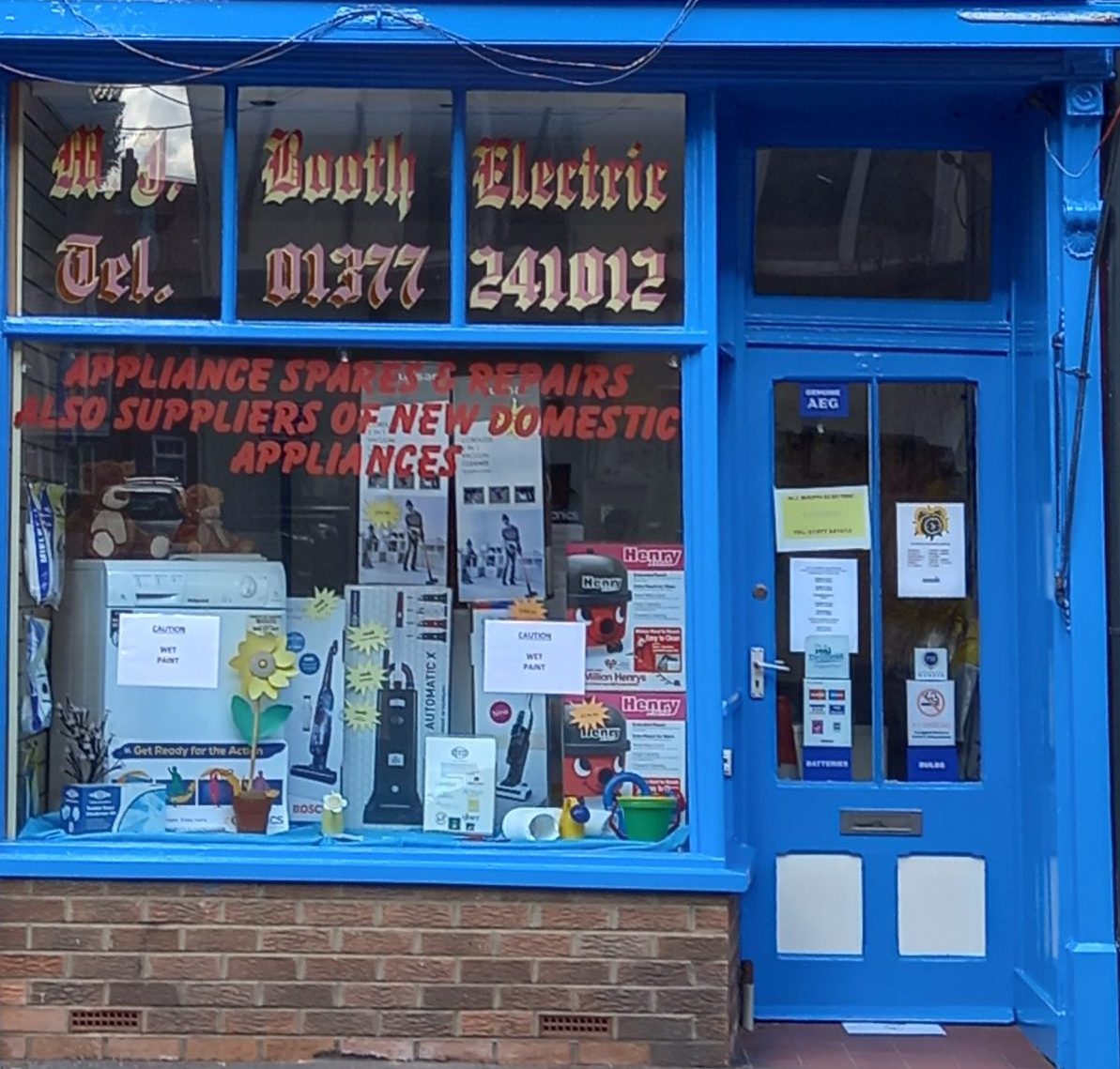 The shop window, lettered Appliance spares and repairs, also suppliers of new domestic appliances, with vacuum cleaners and a washing machine on display